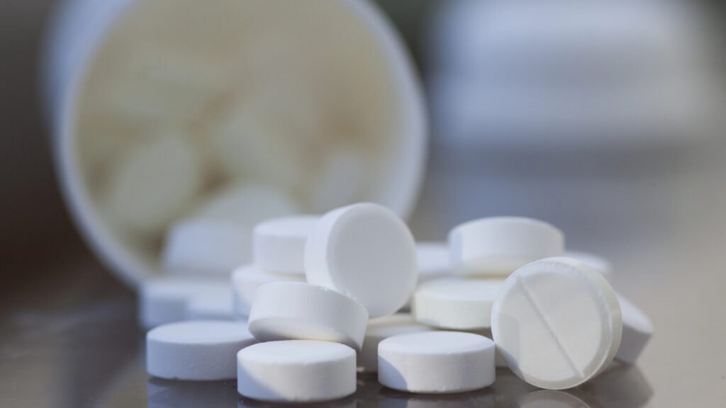 White round tablets scattered from an open bottle on a reflective surface.