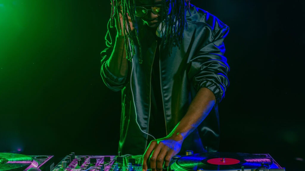 DJ with headphones mixes music on a turntable in a dimly lit setting with green lighting.