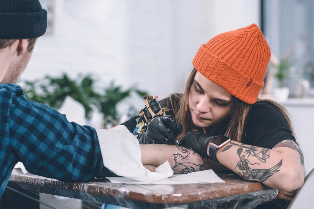 Young man and female tattoo master during tattooing process in studio