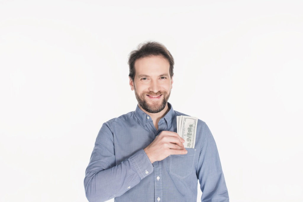 Portrait of cheerful bearded man with dollar banknotes in pocket isolated on white