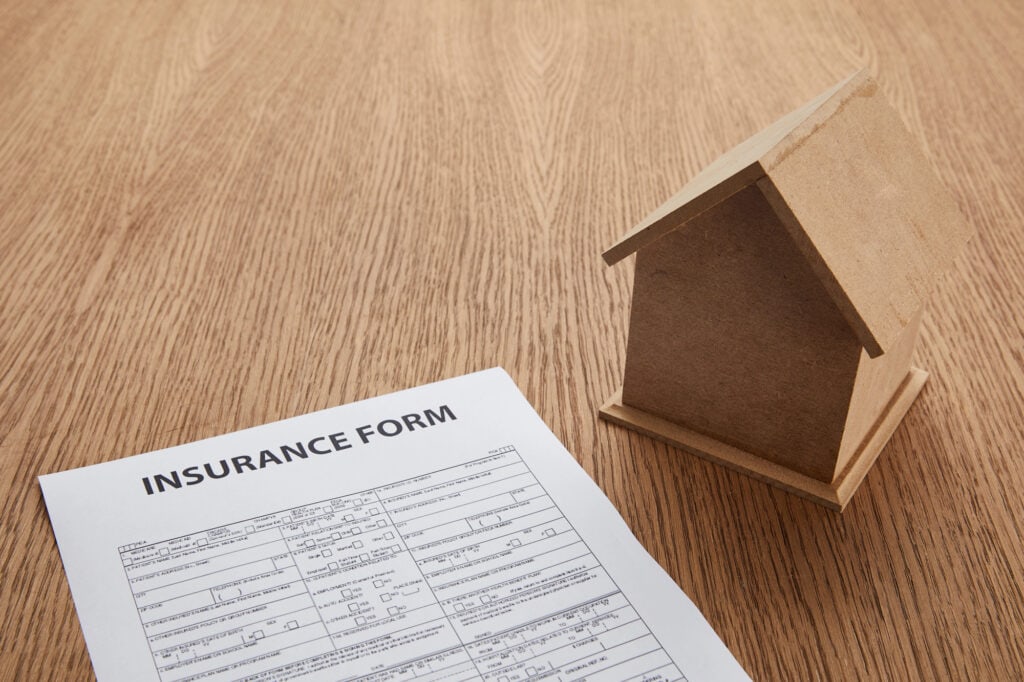 Insurance form and small house model on wooden table with copy space