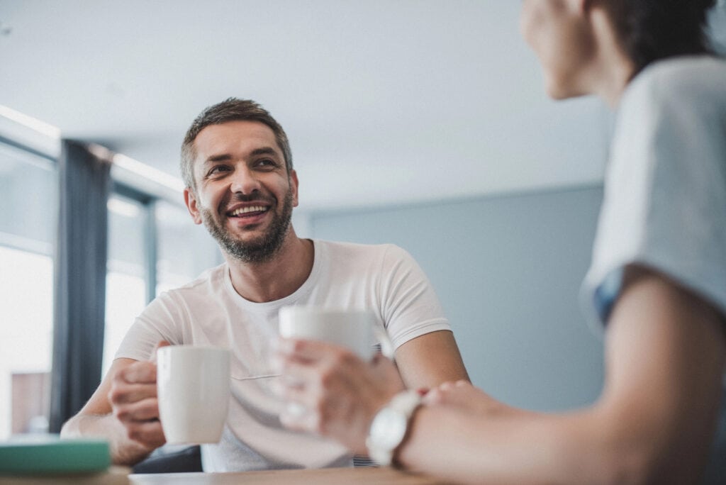 Low angle view smiling couple drinking coffee and talking at table at home