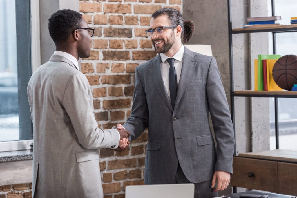 businessman and african american partner shaking hands in office