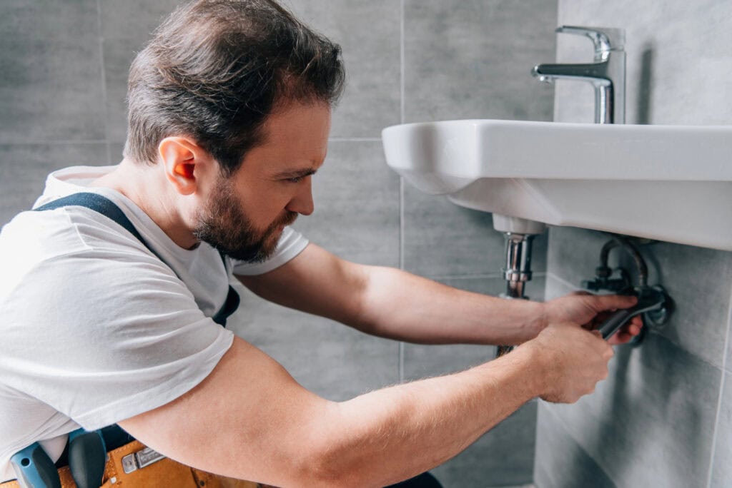 Plumber in working overall fixing sink in bathroom