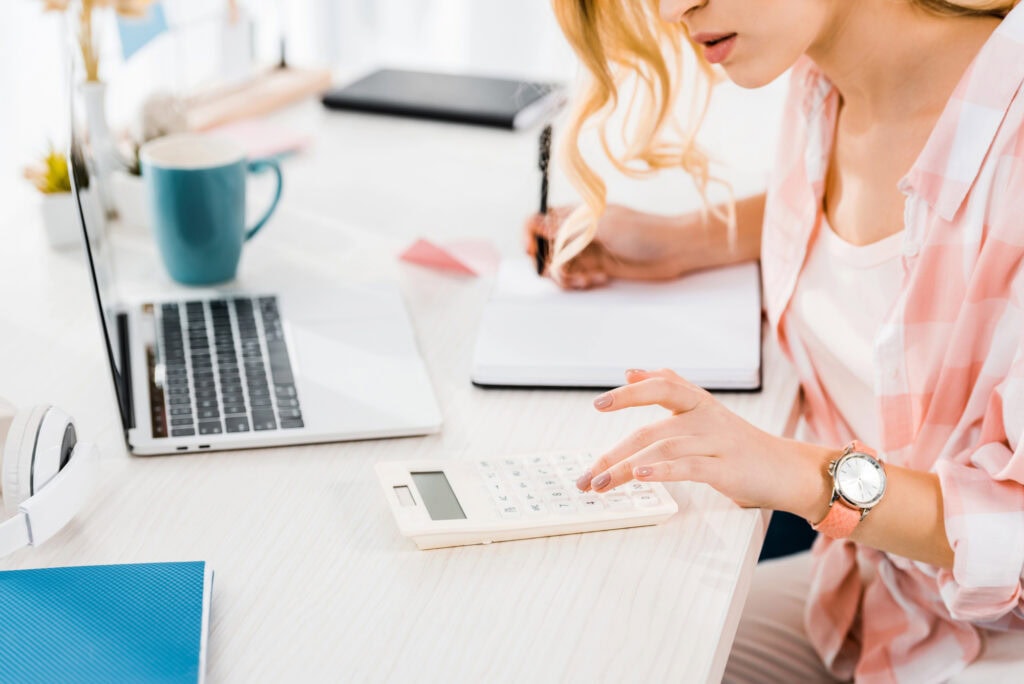 Partial view of woman using calculator and writing in notebook