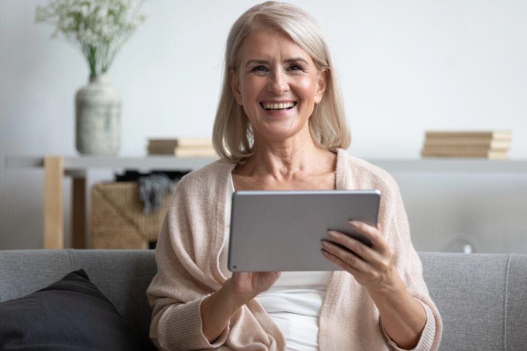 Smiling elder woman using computer tablet at home.