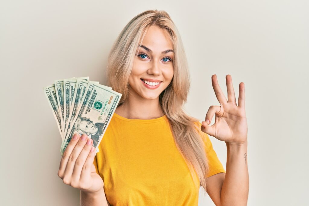 Woman holding 20 dollars banknotes doing ok sign
