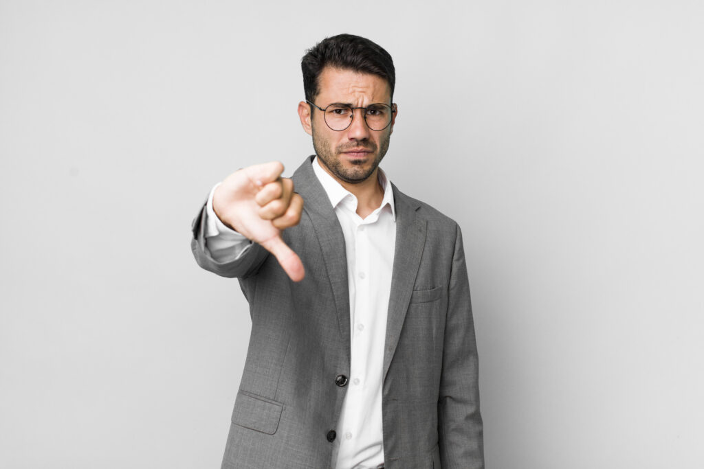 Man in a gray suit and glasses giving a thumbs-down gesture against a plain background.