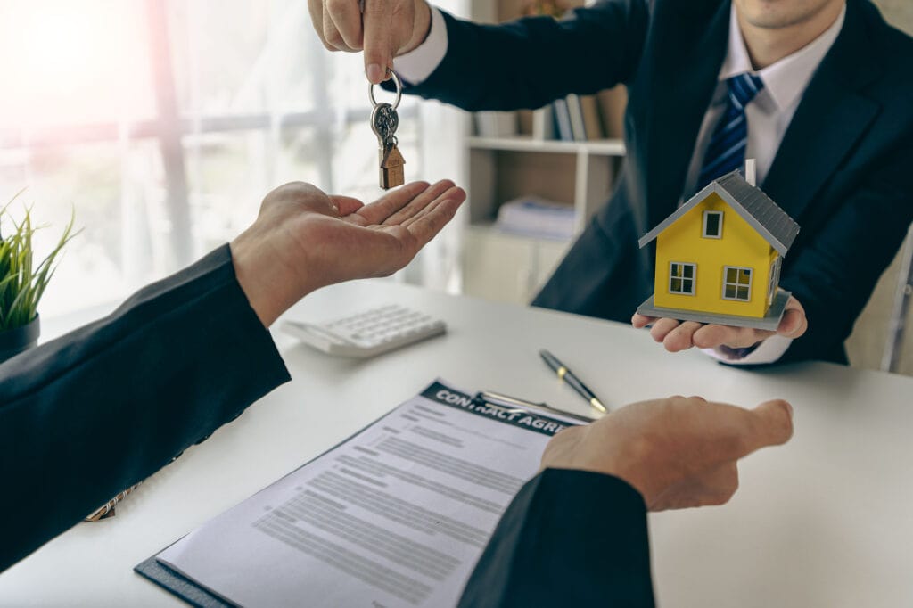 Mortgage Broker hand out keys from new homes to office clients with examples of homes laid out in front.