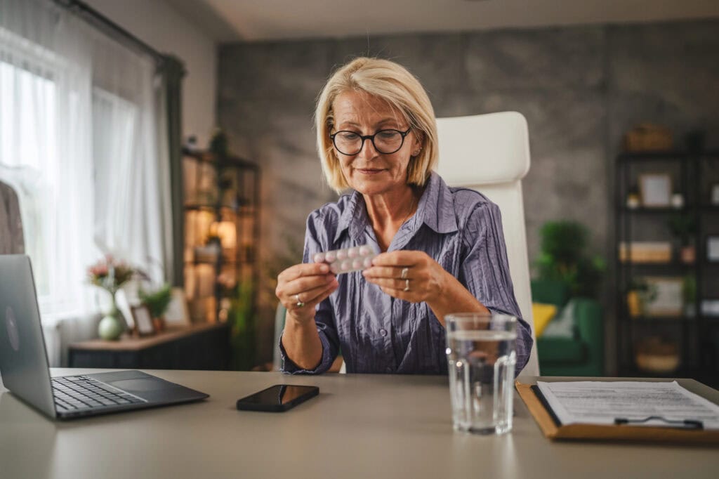 Elder woman drink the medicine with glass of water and work from home