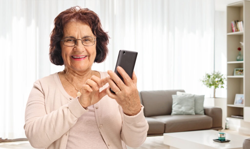 Elderly woman using a phone at home and smiling.