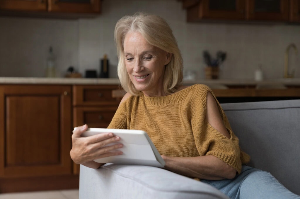 Senior woman using tablet computer, resting on couch.