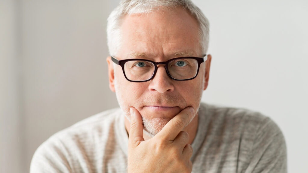 A man with glasses and a grey shirt is looking at the camera.