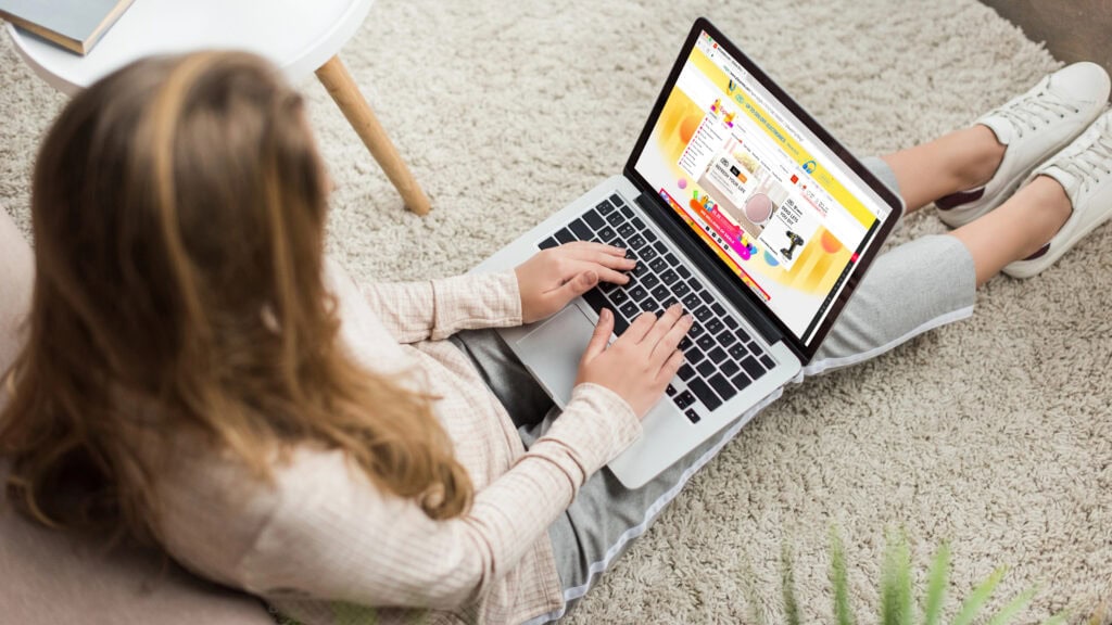 Woman at home sitting on floor and using laptop with aliexpress website on screen