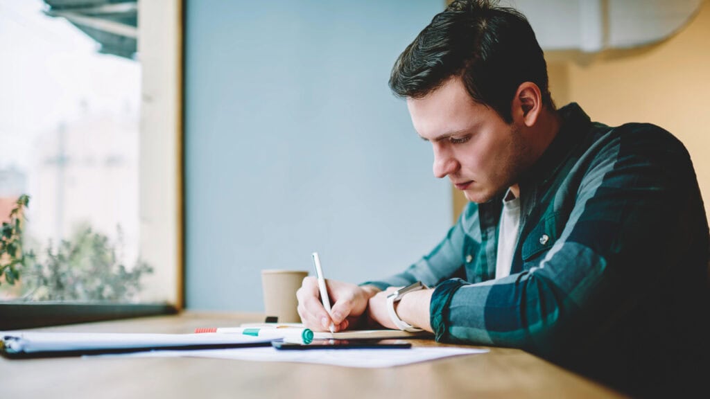 man concentrated on work is writing something while working from home