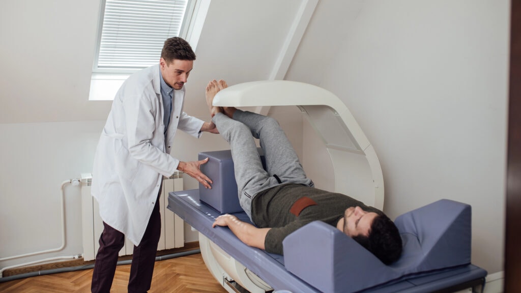 medical technician operating the bone densitometer while his patient is lying on the bed.