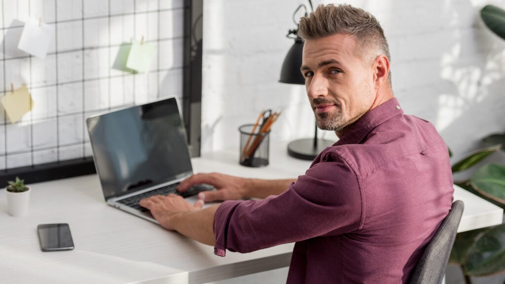 Man sitting at table with laptop and smartphone at home office