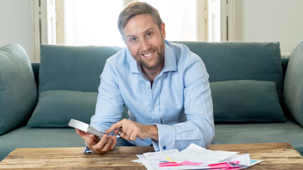 business man accounting costs, charges, taxes and mortgage on sofa at home with credit card and calculator