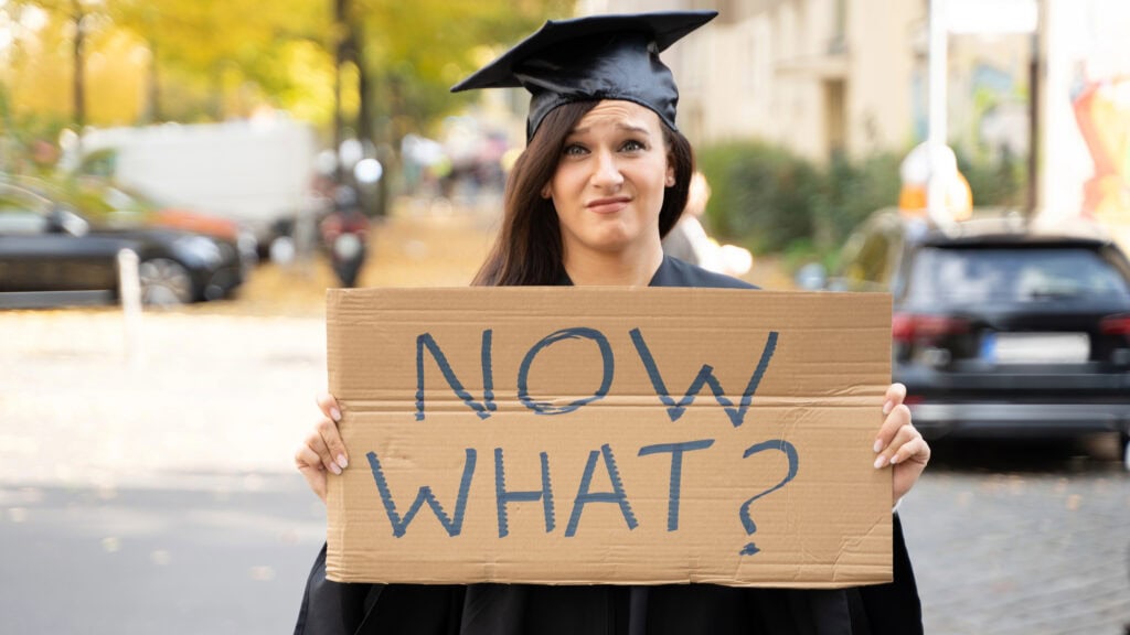 Sad Graduate Student Standing With Now What Placard On Street