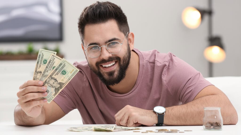 Happy young man with money at white table indoors