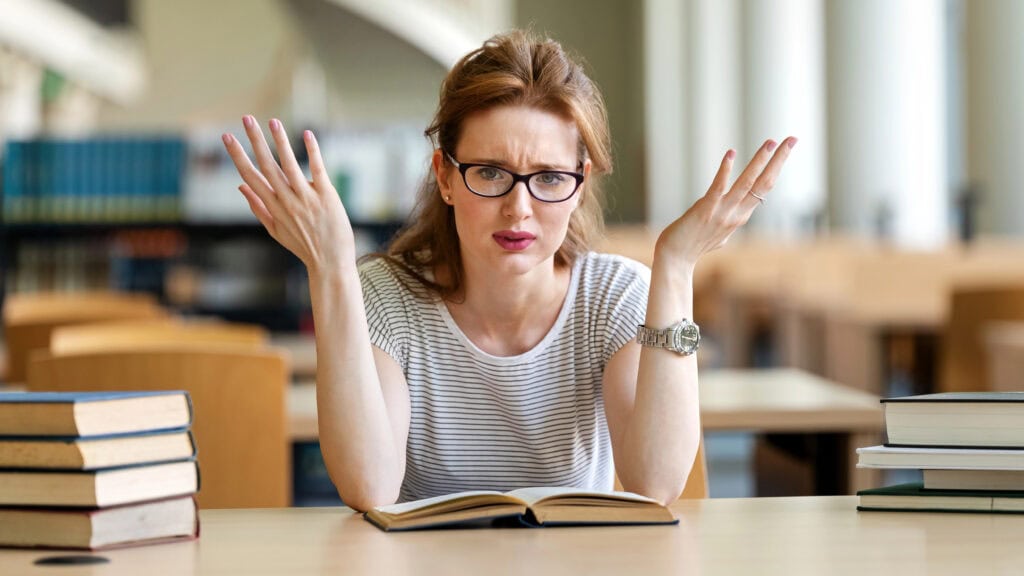 Exhausted young tired female studying and preparing for exam in college library
