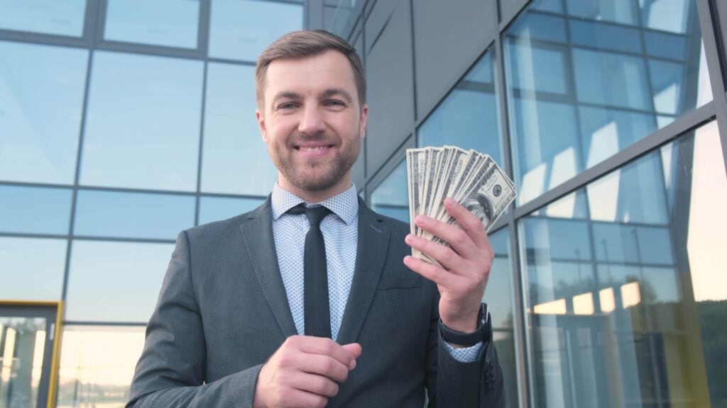 Portrait of a smiling young man, banker, businessman, holding a stack of American dollars. Big salary. Business income.
