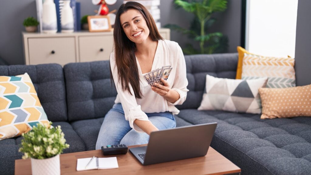 Woman using laptop counting dollars at home