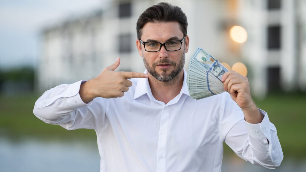 Man is holding dollar money in one hand, outdoor setting, outside house.
