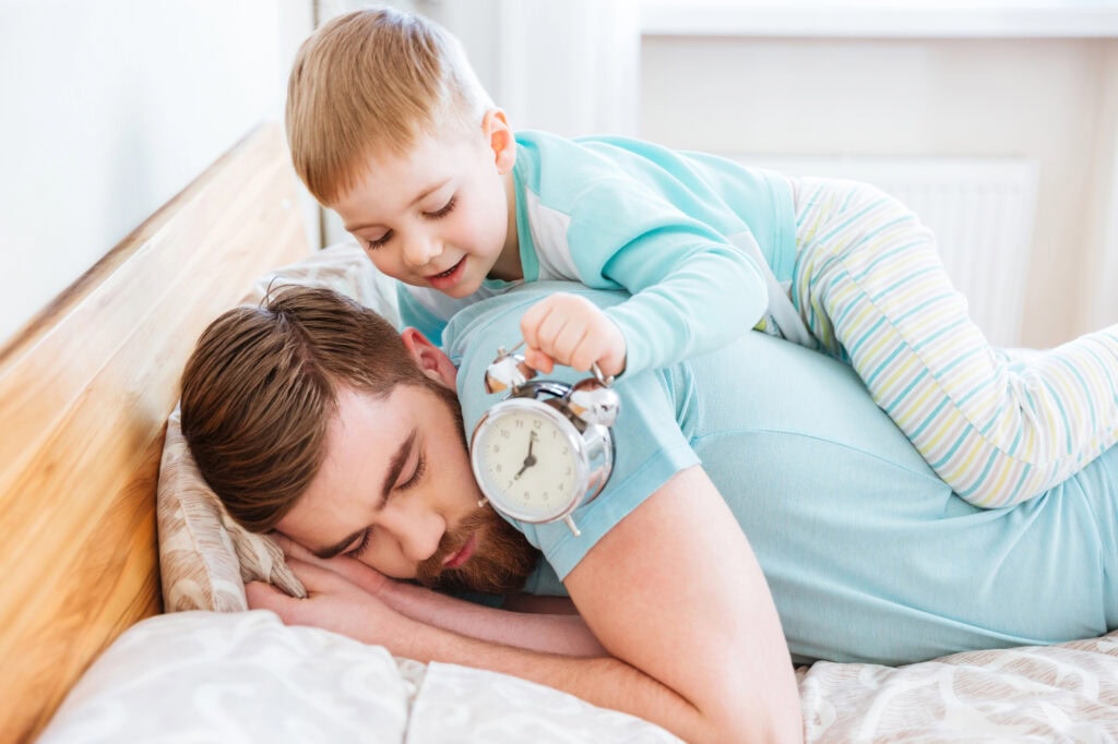 Little son holding alarm clock near sleeping father ear
