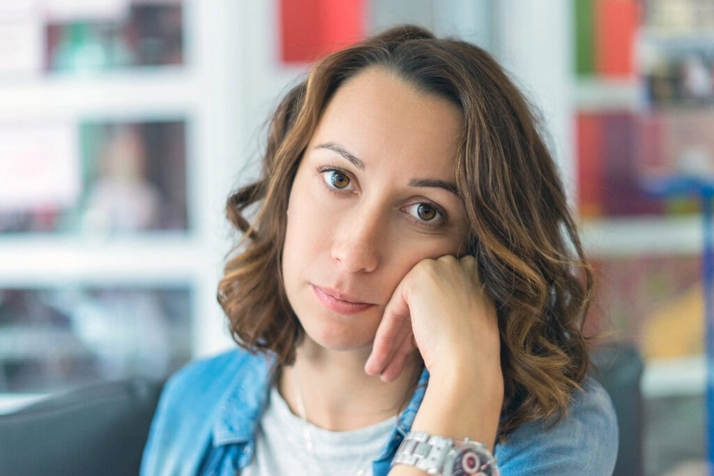 Girl sits in at home, hand on the cheek.