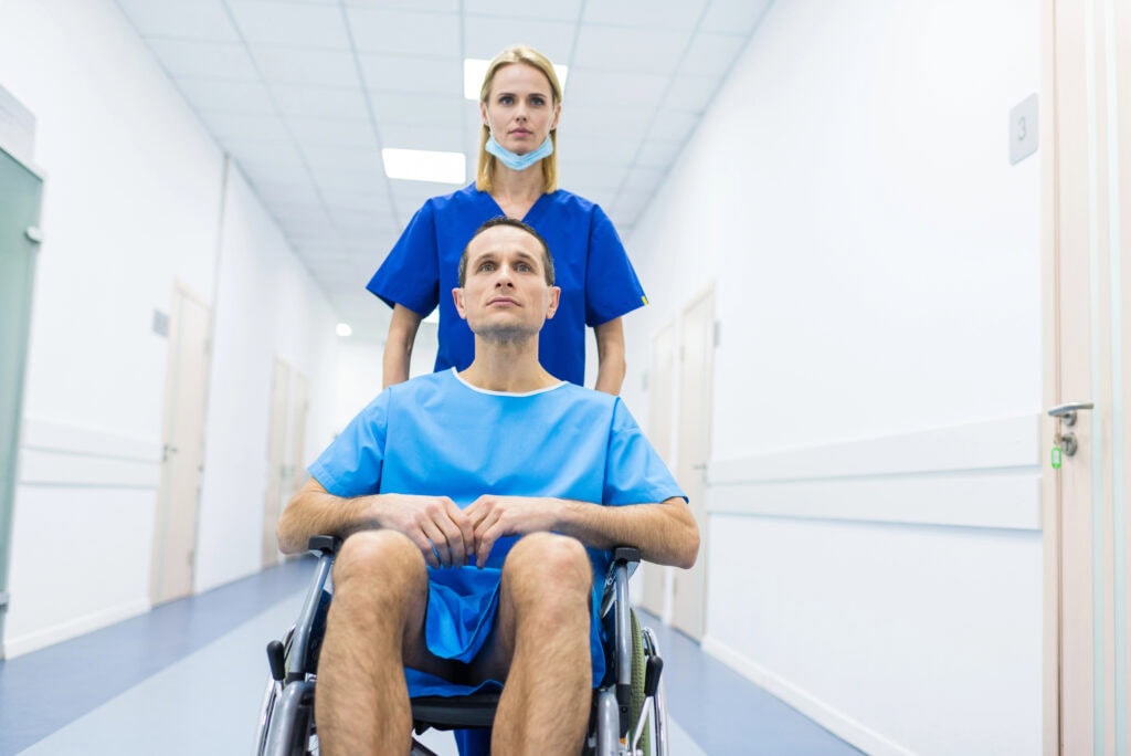 Female surgeon and male patient in wheelchair in hospital corridor