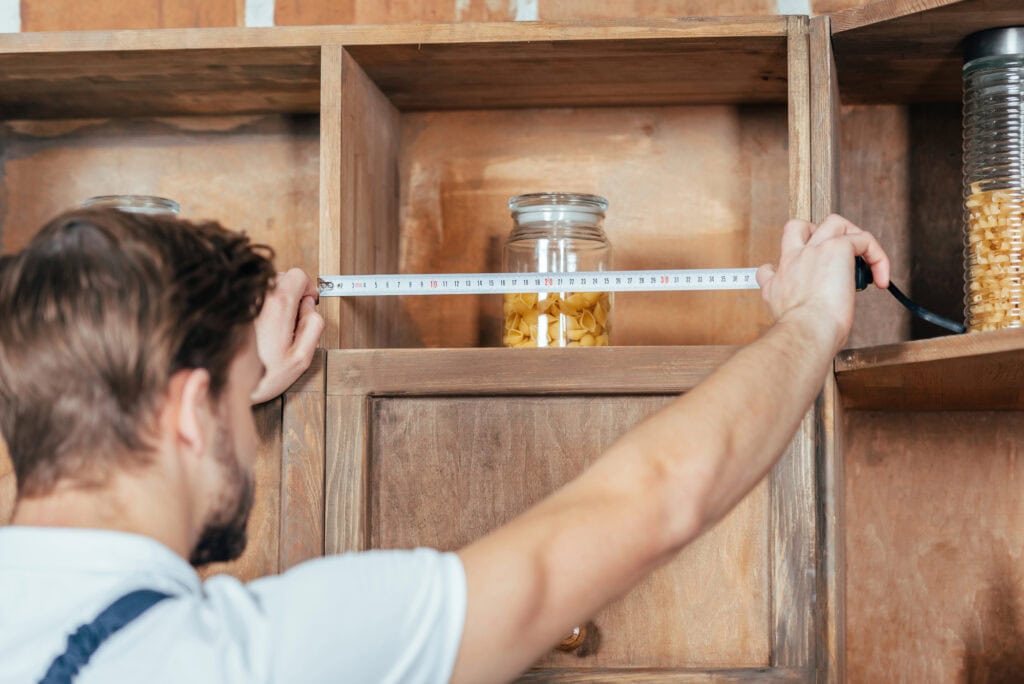 Selective focus of young handyman measuring kitchen furniture with tape