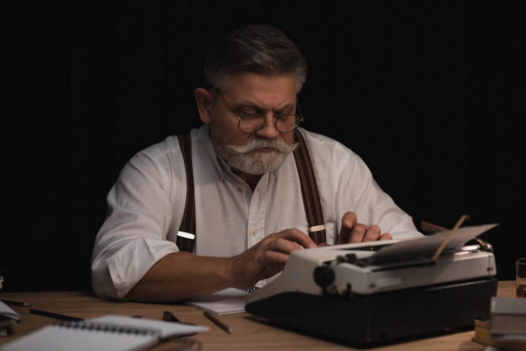 Senior writer working with typing machine isolated on black