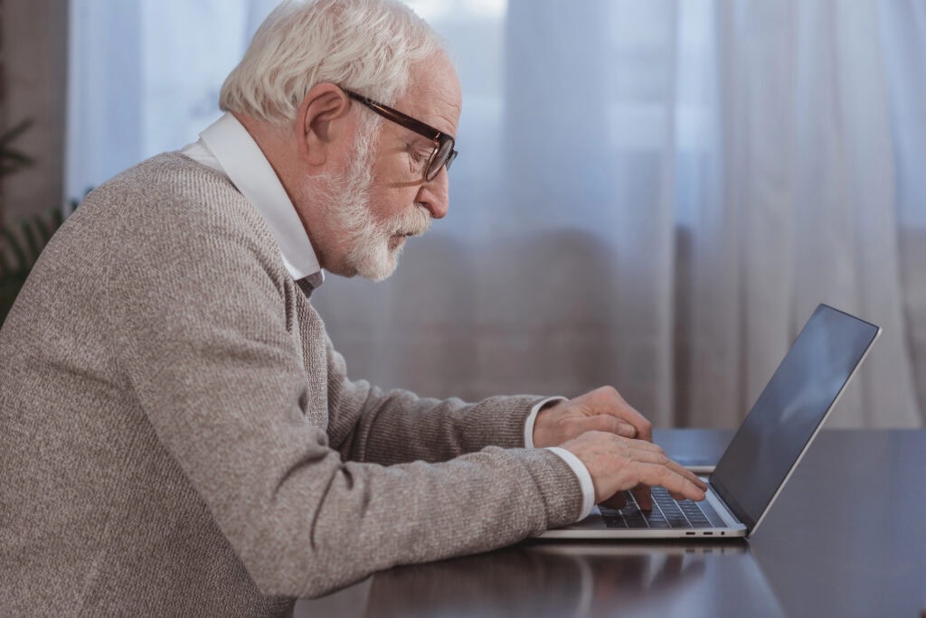 Side view of handsome grey hair man using laptop at home