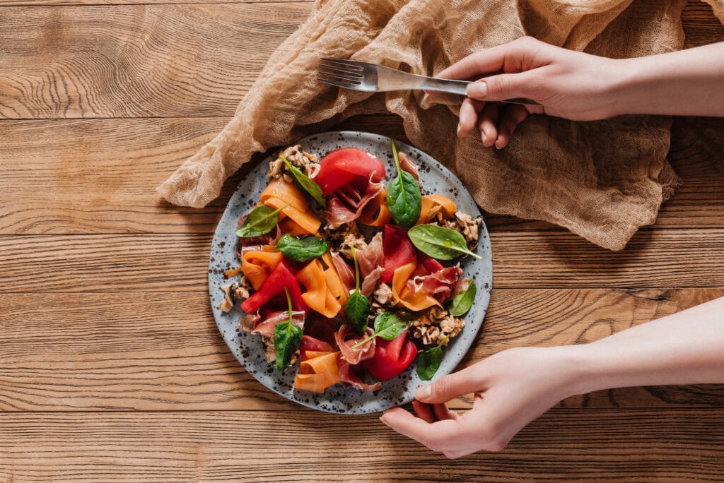 Person holding fork and plate with salad with mussels, vegetables and jamon