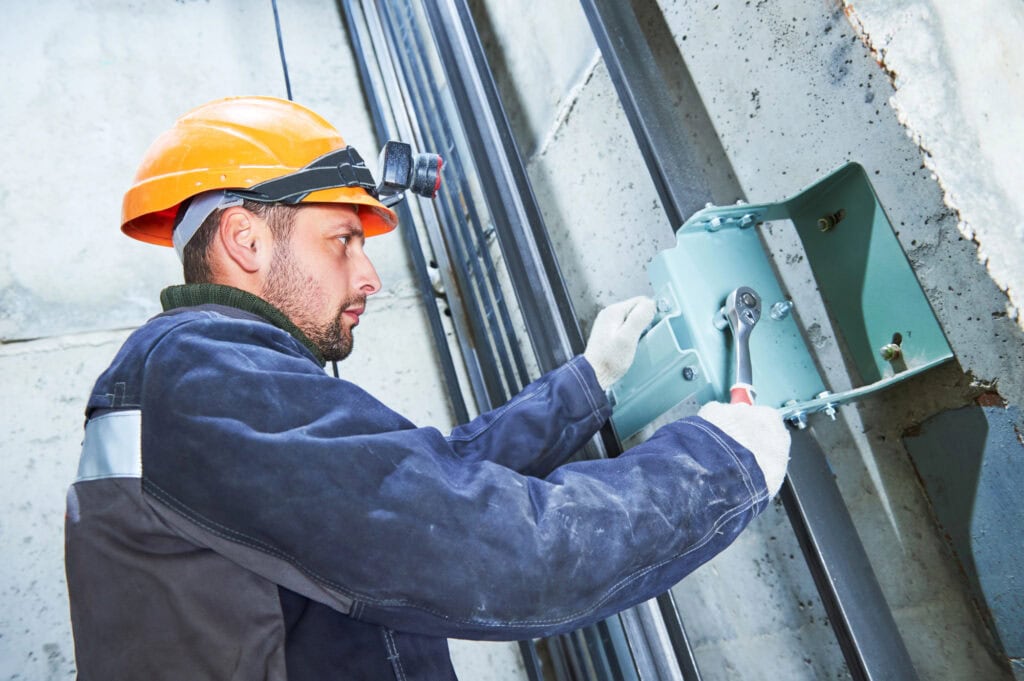 Machinist with spanner adjusting lift mechanism in elevator shaft