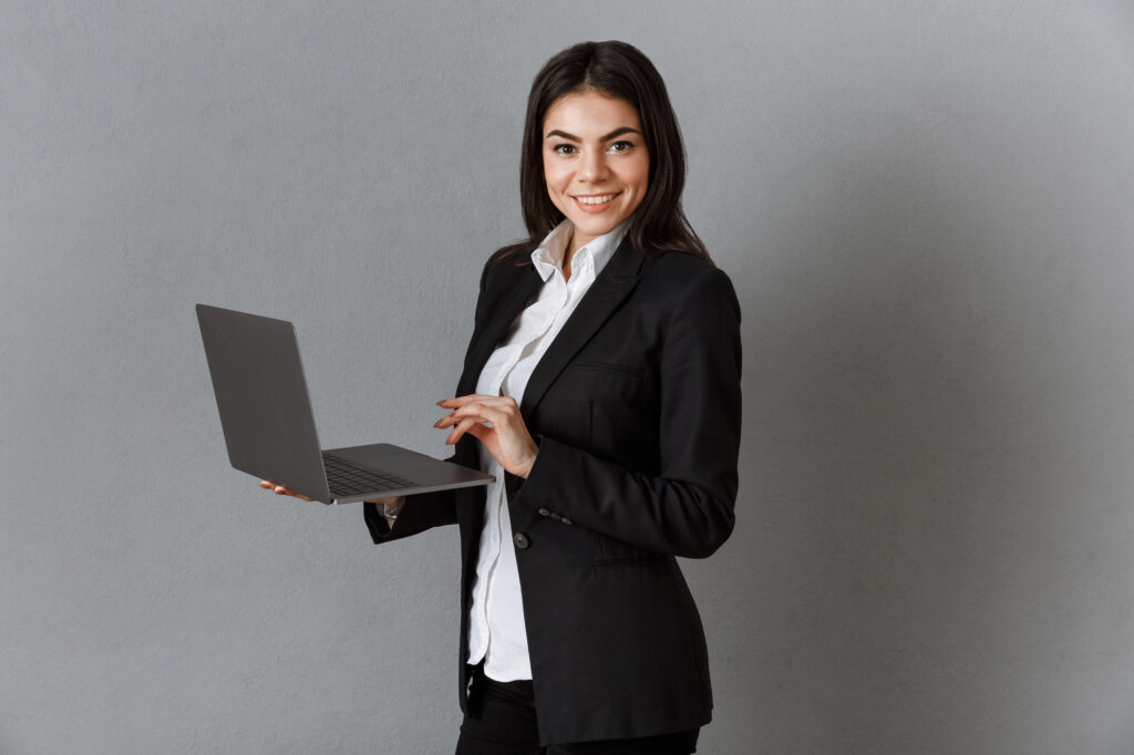 Side view of smiling businesswoman with laptop against grey wall background