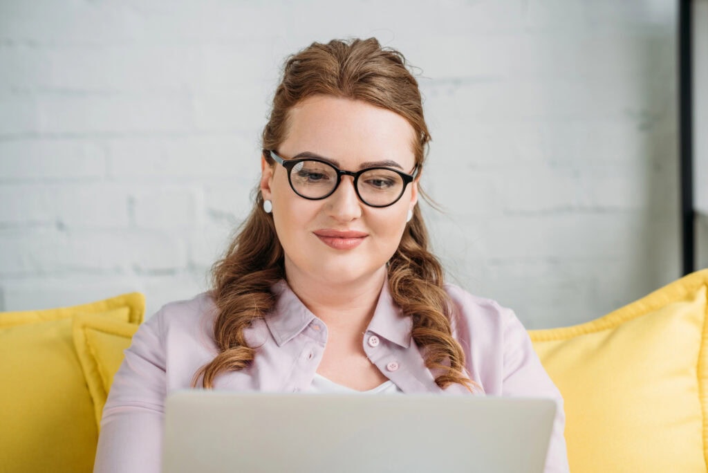 Beautiful freelancer sitting with laptop on sofa at home