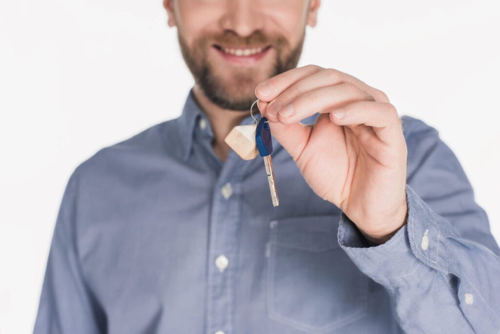 Cropped shot of smiling man showing key from new house in hand isolated on white