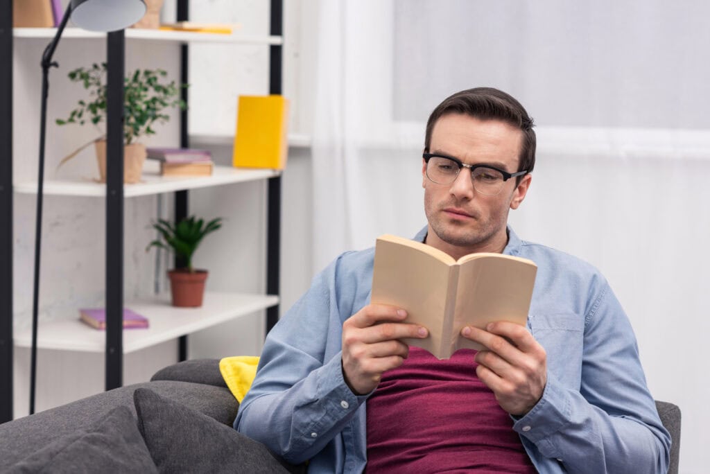 Concentrated adult man reading book on couch at home