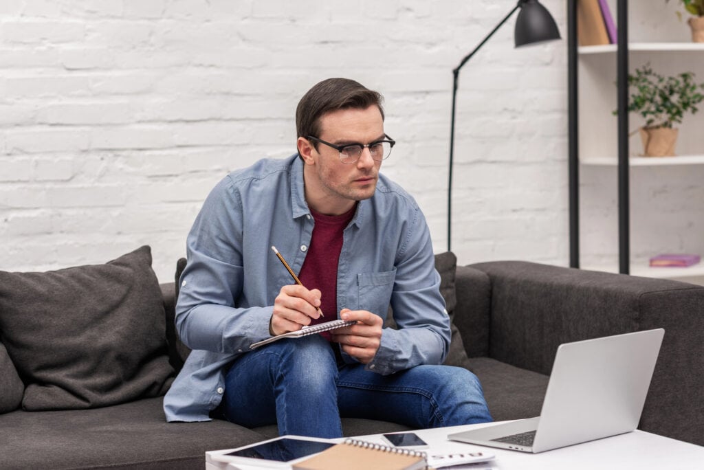 Focused adult man writing notes and looking at laptop