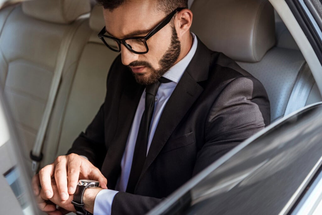 Handsome businessman in suit checking time on wristwatch in car