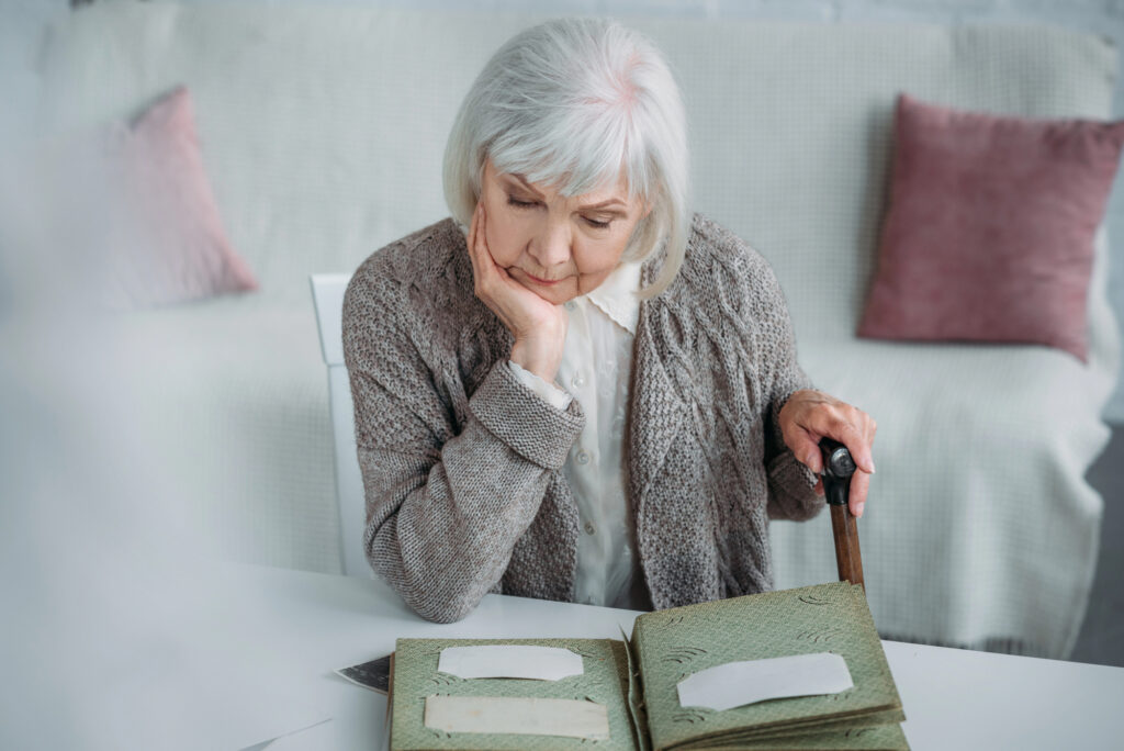 Portrait of grey hair woman looking at photos in photo album at table at home