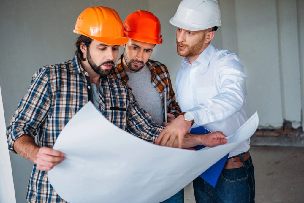 Group of adult architects with blueprint having conversation inside of constructing building