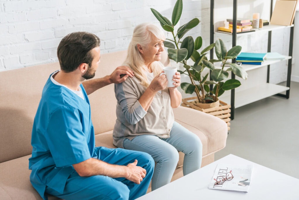 High angle view of social worker looking at smiling senior woman drinking tea