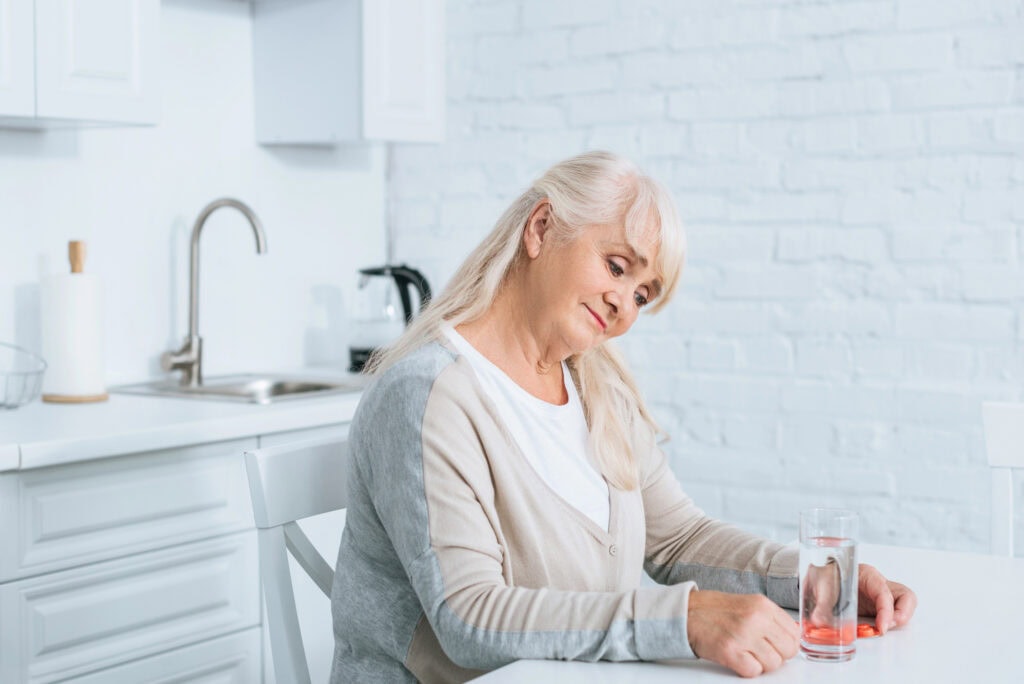 Senior woman sitting at table and holding pills