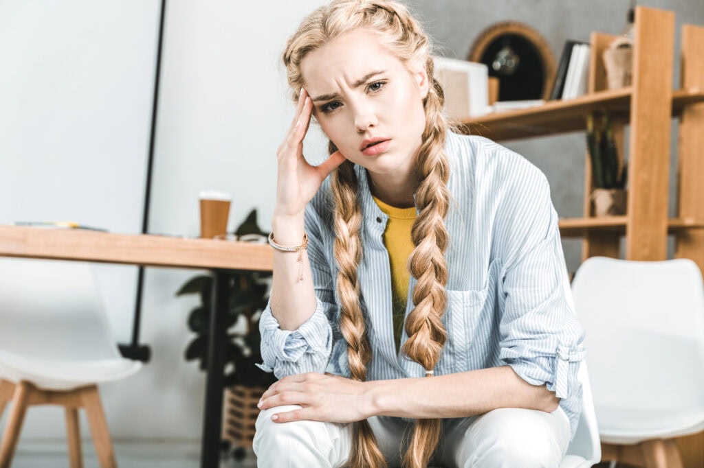 Portrait of young pensive businesswoman sitting at workplace in office and looking at camera