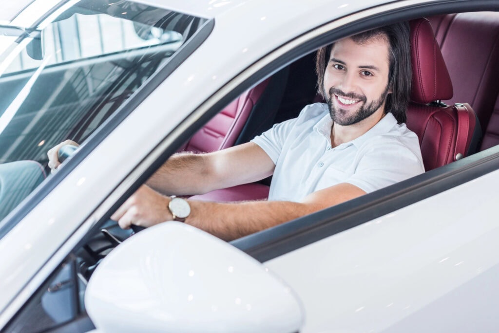 Smiling bearded man sitting in new car for test drive in dealership salon