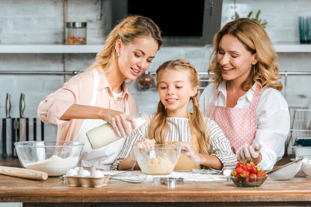 Smiling child with mother and grandmother making dough together at home