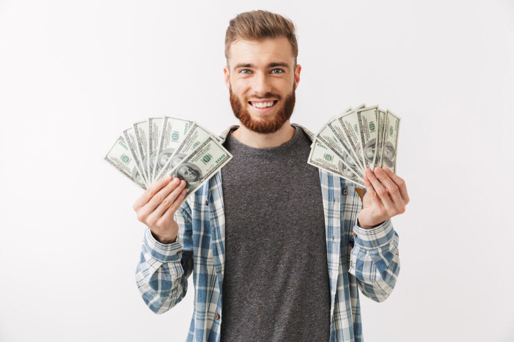 Portrait of a cheerful young bearded man standing isolated over white, showing money banknotes